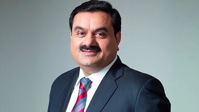Indian businessman with a mustache in a dark suit and striped tie, smiling at the camera.