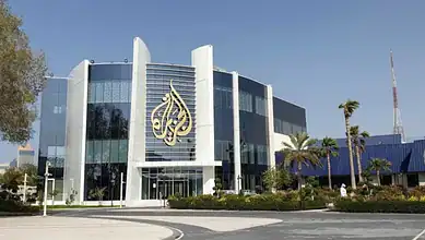 Modern Al Jazeera headquarters with glass facade and logo in a sunny setting.