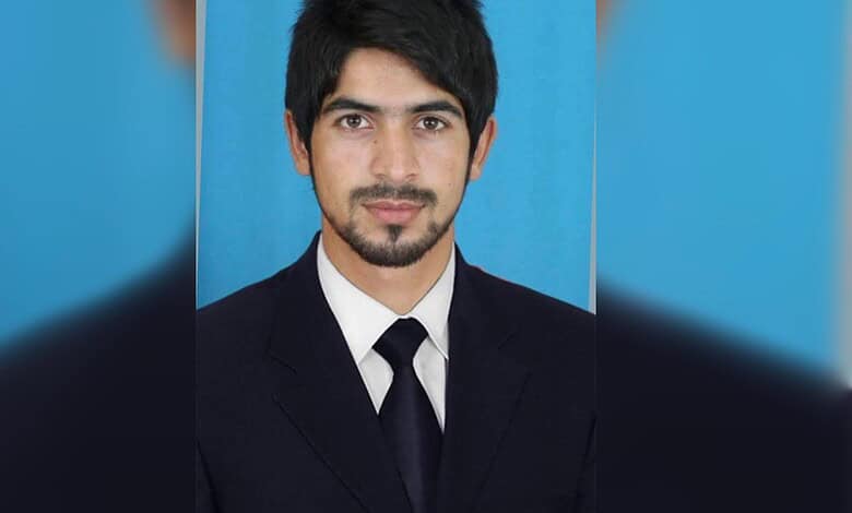 Young man in formal suit with a blue background, looking confidently at the camera.
