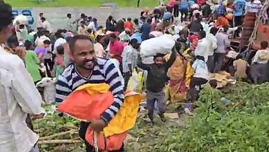 Crowd of people stealing apples from a lorry on the roadside in a busy area.