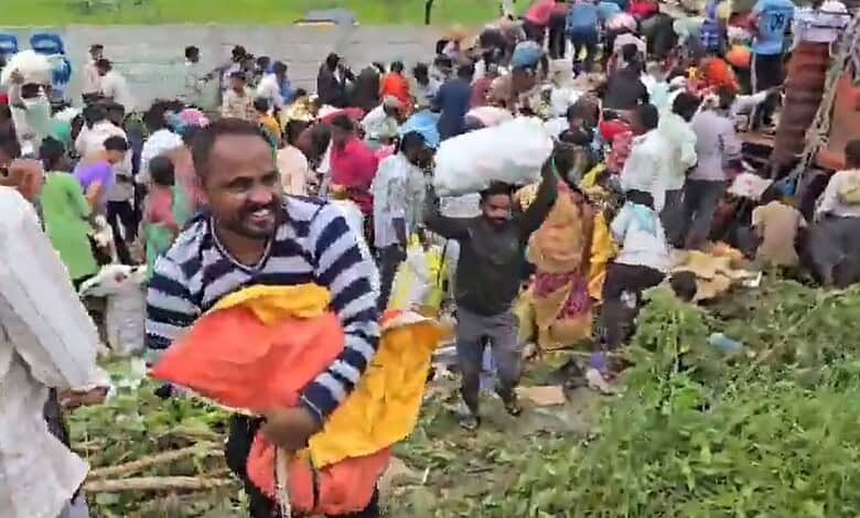 Crowd of people stealing apples from a lorry on the roadside in a busy area.