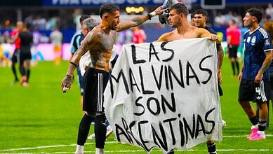 Football players holding a banner that reads 'Las Malvinas Son Argentina' during a match.