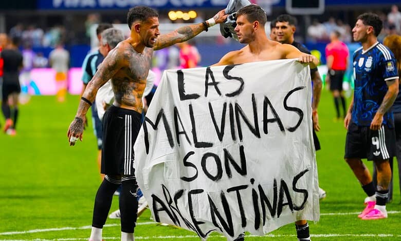 Football players holding a banner that reads 'Las Malvinas Son Argentina' during a match.