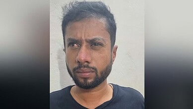 Man with beard and serious expression against plain wall.