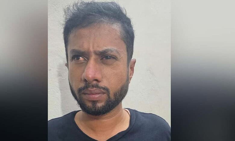Man with beard and serious expression against plain wall.