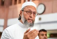 Owaisi speaking passionately, wearing white traditional attire and glasses, in a public setting.