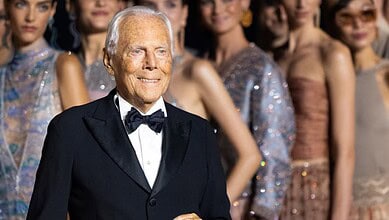 Bille August smiling at a fashion event with models in the background.
