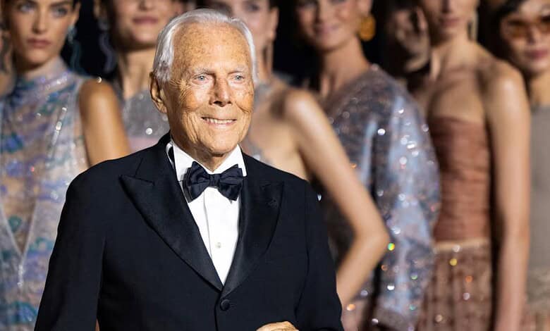 Bille August smiling at a fashion event with models in the background.
