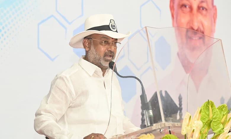 Bandi Sanjay speaking at a public event with a microphone and a transparent shield.
