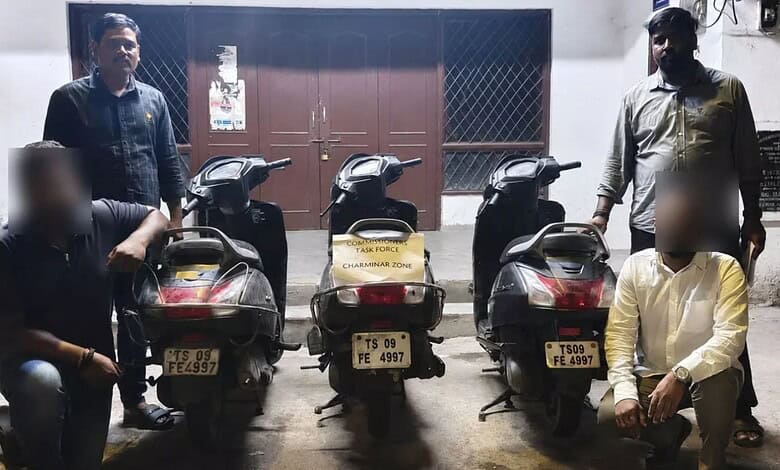 Three scooters with similar number plates parked in front of a building with four men standing nearby.