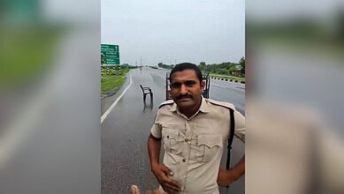 Telangana excise constable standing on a wet road with a chair in the background.