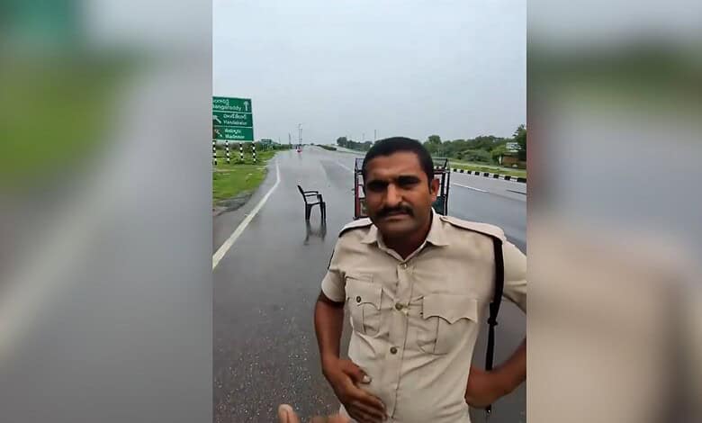 Telangana excise constable standing on a wet road with a chair in the background.
