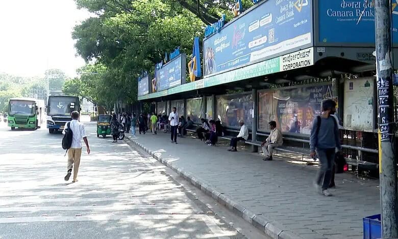 Bus stop near traffic signals in Bengaluru with people waiting and walking nearby.