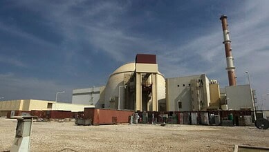 Iran's Bushehr nuclear power plant with cooling tower and reactor building under a blue sky.