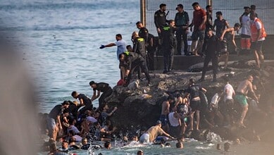 Group of migrants and authorities on rocky shoreline during crossing into Spain from Morocco.