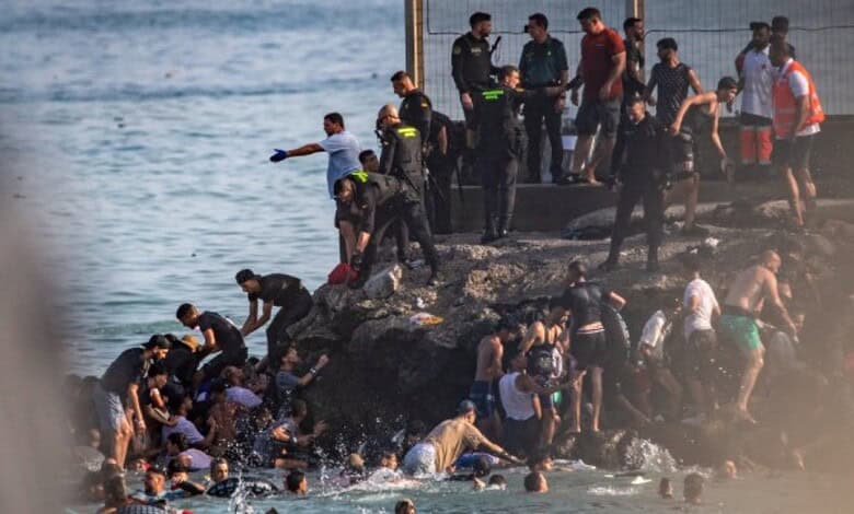Group of migrants and authorities on rocky shoreline during crossing into Spain from Morocco.