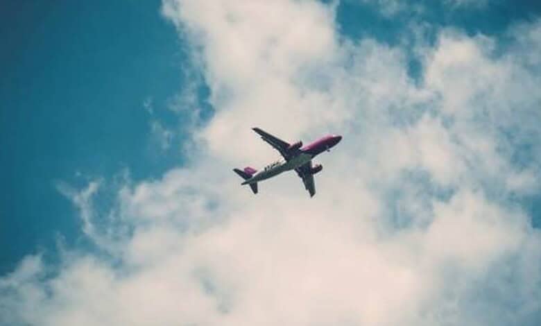 A commercial passenger aircraft flies overhead against a blue sky filled with large white clouds.