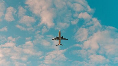 Passenger airplane flying high in the sky with clouds below, symbolising air travel and airline services.