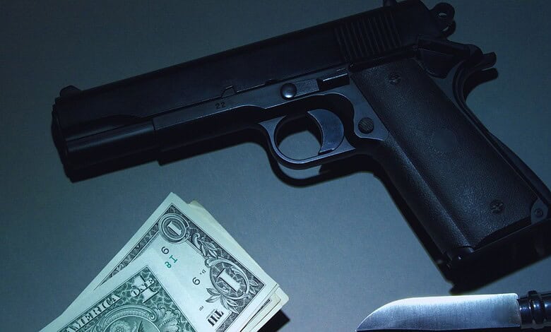 Handgun, cash, and knife arranged on a dark surface, evoking crime or danger.