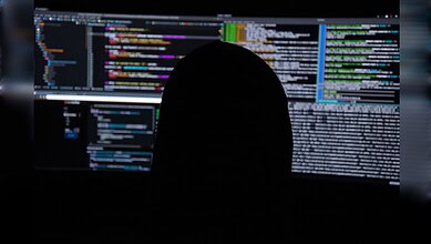 Person analyzing code on multiple screens for cybersecurity threats.