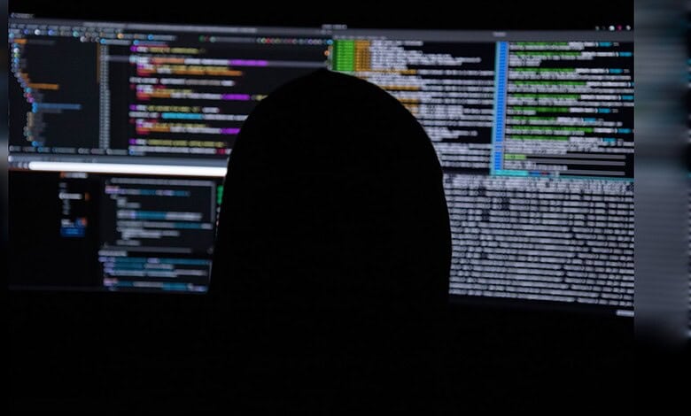 Person analyzing code on multiple screens for cybersecurity threats.