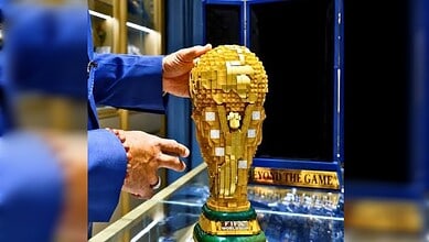 Person holding a large Lego trophy resembling a World Cup, made of gold-coloured Lego bricks.