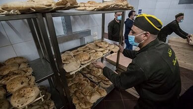 Officials inspecting bread loaves in a bakery, wearing masks and uniforms, in Egypt.