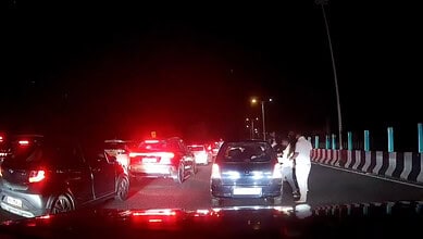 Multiple cars stopped on the Bengaluru-Mysuru Expressway at night with a person standing outside a car.