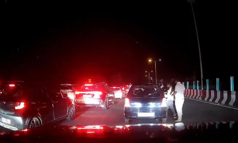 Multiple cars stopped on the Bengaluru-Mysuru Expressway at night with a person standing outside a car.