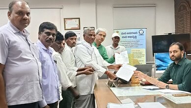 Group of men receiving documents from a man at a desk in an office setting.