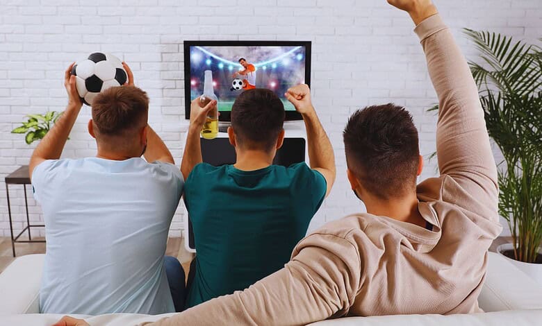 Three young men cheering and celebrating while watching a football game on TV.