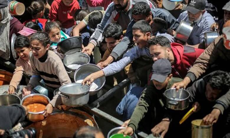 Crowd of people, including children, waiting in line for food distribution in Gaza amid severe food inseu.