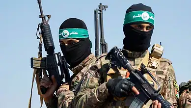 Two armed Palestinian militants in camouflage uniforms and black masks, holding rifles.