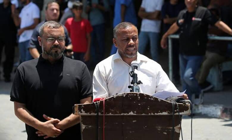 Man speaking at a podium during an outdoor gathering with crowd in background.