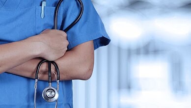 Close-up of a healthcare worker in blue scrubs holding a stethoscope.
