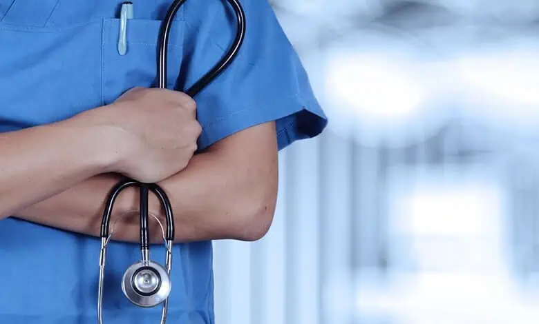 Close-up of a healthcare worker in blue scrubs holding a stethoscope.