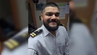 Smiling Indian marine engineer in uniform after ship attack recovery, in office setting.