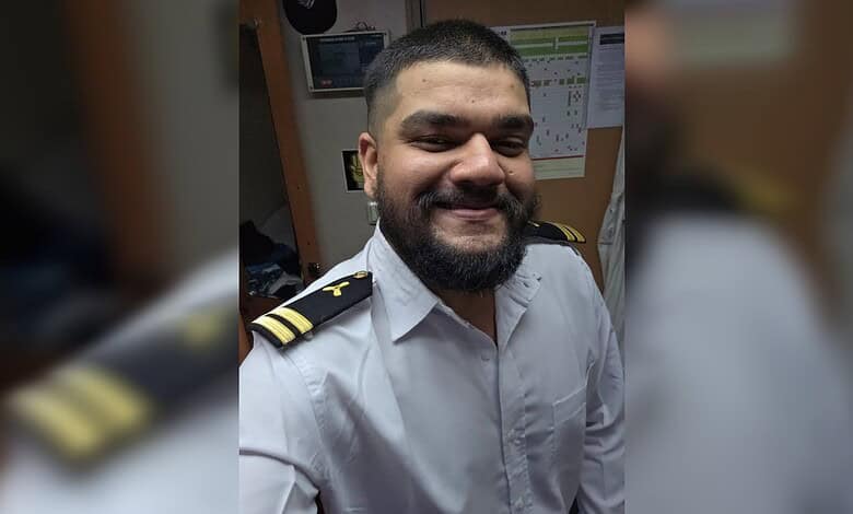 Smiling Indian marine engineer in uniform after ship attack recovery, in office setting.