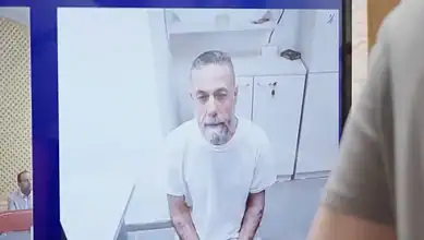 Hussam Abu Safiya appears on a courtroom video screen during a remote hearing, seated in a detention room wearing a white T-shirt.
