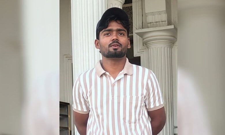 Young man in striped shirt standing outside with columns in background.