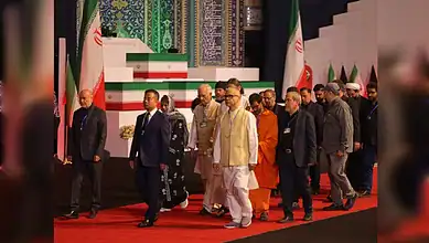 Indian delegation in formal attire pays tribute at a memorial event with Iranian flags in the background.
