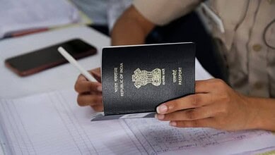 A person holds an Indian passport while completing paperwork at a service desk, representing passport and consular services.