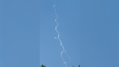 A bright lightning bolt streaks across a clear blue sky during daytime.