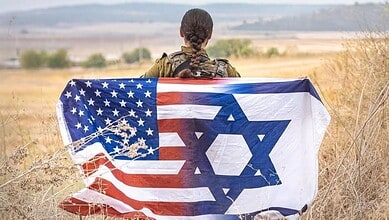 Soldier holding a flag combining the US and Israeli flags in a dry field.