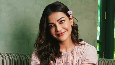 Kajal Aggarwal smiling in a pink outfit with floral accessories in her hair.
