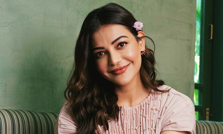 Kajal Aggarwal smiling in a pink outfit with floral accessories in her hair.