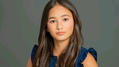 Portrait of a young girl with long brown hair and a neutral expression.