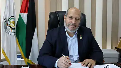 Khalil al-Hayya sitting at desk with Palestinian flags in background.