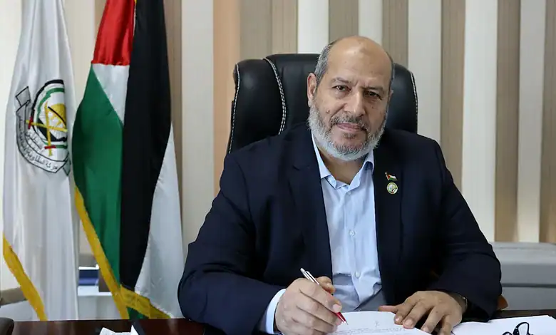 Khalil al-Hayya sitting at desk with Palestinian flags in background.