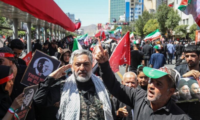 Crowd of protesters in Mashhad holding flags and banners during a demonstration.